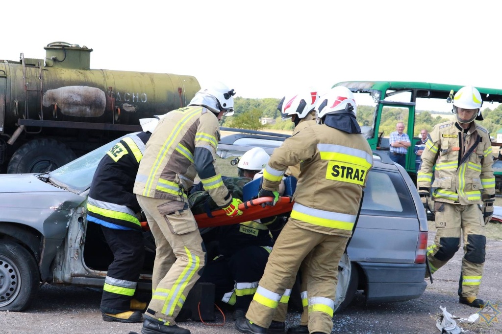 Na zdjęciu widzimy symulację wypadku drogowego. Ze zniszczonego wskutek wypadku auta grupa strażaków ewakuuje osobę poszkodowaną.