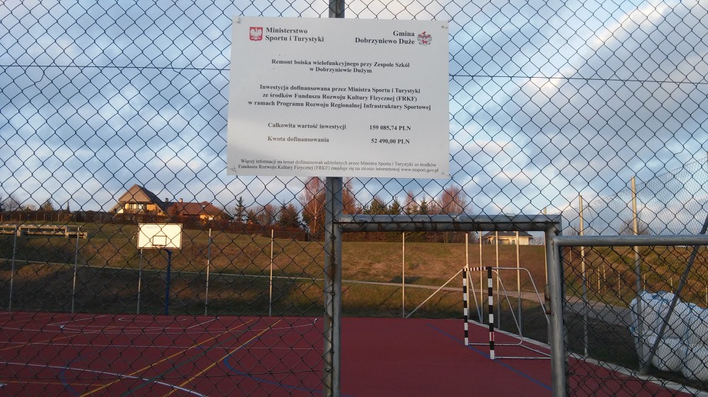 Zdjęcie przedstawia boisko w Dobrzyniewie Dużym. Na pierwszym planie widzimy tablicę informacyjną, w tle boisko