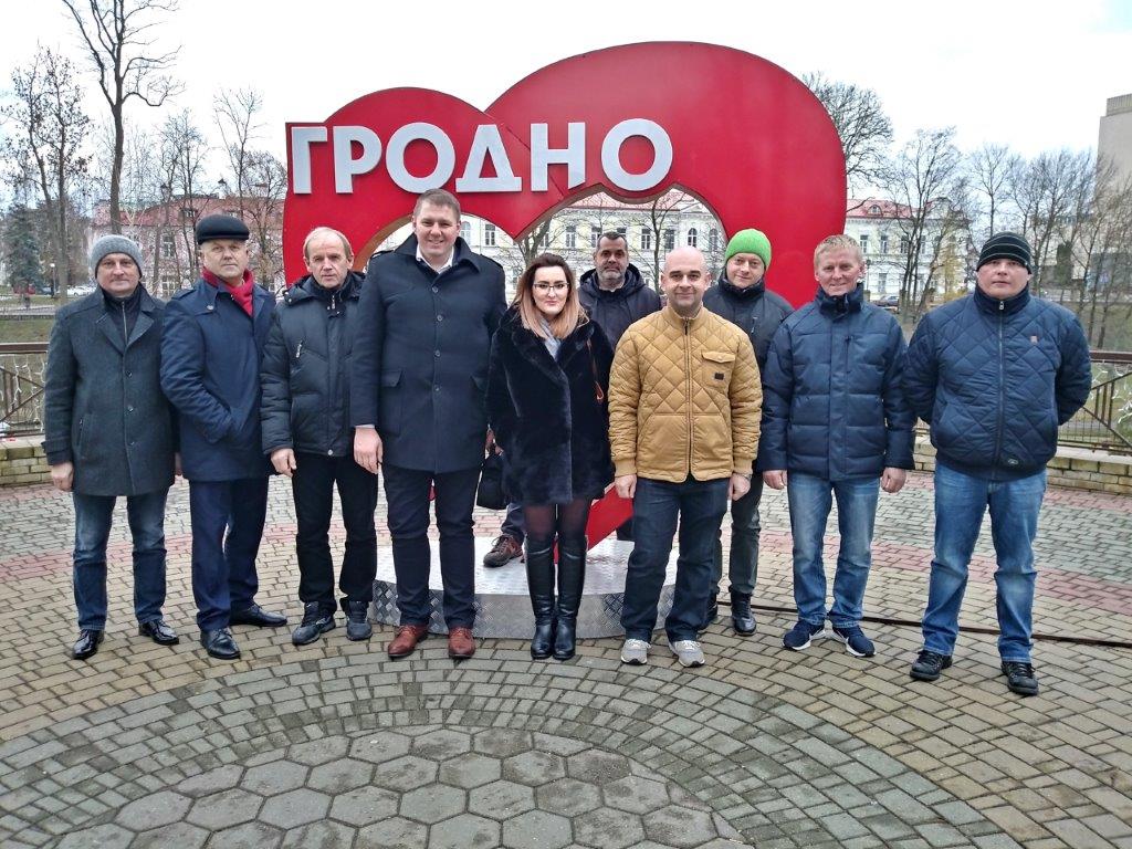 Na zdjęciu widzimy grupę osób, kobietę i mężczyzn. Stoją wspólnie pozując do grupowego zdjęcia, w tle widać napis w języku Białoruskim / Rosyjskim.