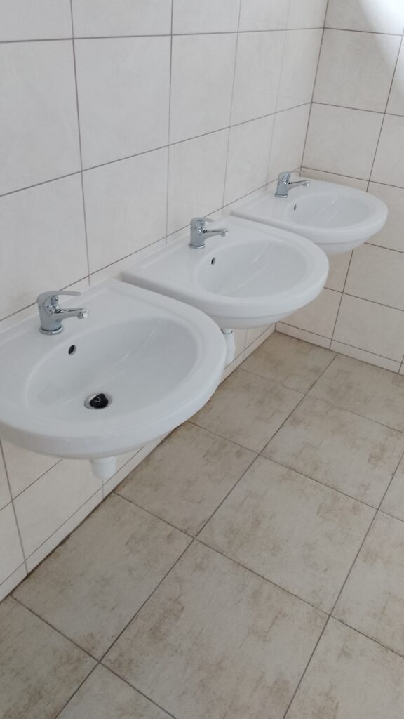 Trzy białe umywalki z bateriami w łazience z jasną glazurą.