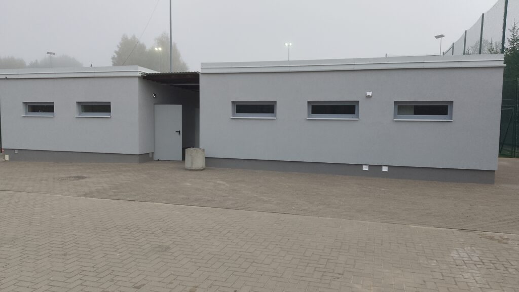Budynek sanitarno szatniowy z jasnoszarą elewacją i poziomymi oknami